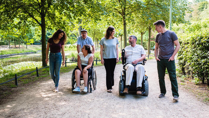 Eine Gruppe Menschen mit und ohne Behinderung macht einen gemeinsamen Spaziergang in einer Grünanlage.