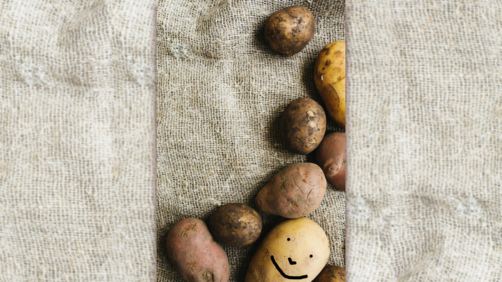 Foto: Eine handvoll Kartoffeln auf Sackleinen, auf eine ist ein lachendes Gesicht gemalt