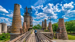 Foto: Hohe Schornsteine im Muesumspark Rüdersdorn an einem sonnigen Tag, in der Bildmitte eine Spaziergängerin von hinten