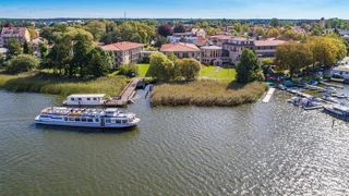 Luftaufnahme vom Seehotel mit dem Grienricksee, auf dem ein kleines Schiff fährt.